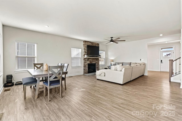 dining room featuring a stone fireplace, ceiling fan, and light wood-type flooring