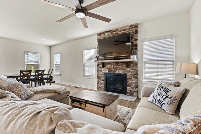 living room featuring ceiling fan, a stone fireplace, and light hardwood / wood-style floors