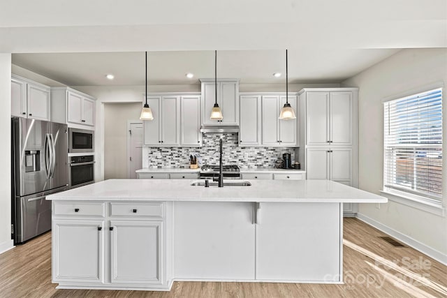 kitchen featuring stainless steel appliances, an island with sink, hanging light fixtures, and white cabinets