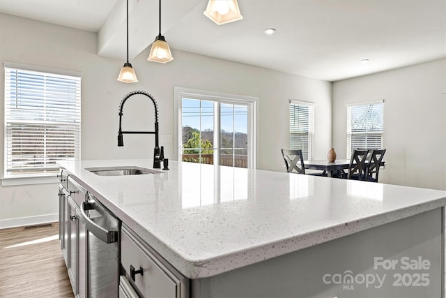 kitchen with light stone counters, decorative light fixtures, sink, and a center island with sink