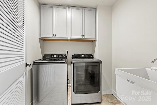 laundry area with sink, light tile patterned floors, washing machine and dryer, and cabinets