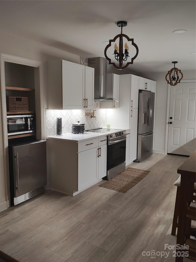 kitchen featuring pendant lighting, white cabinets, appliances with stainless steel finishes, and wall chimney range hood