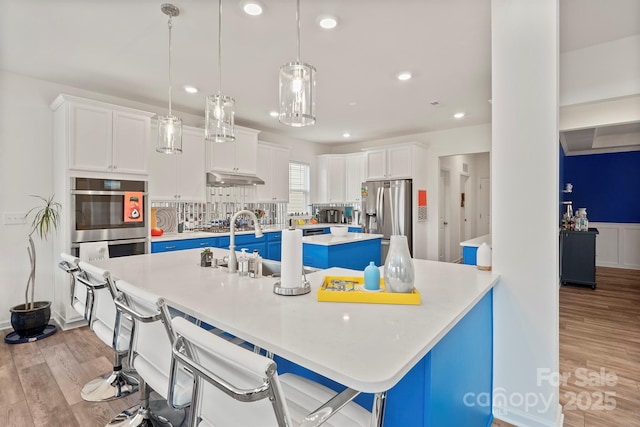 kitchen with hanging light fixtures, white cabinetry, appliances with stainless steel finishes, and a breakfast bar