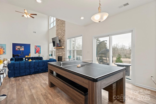 rec room featuring ceiling fan, a towering ceiling, a fireplace, and light hardwood / wood-style floors