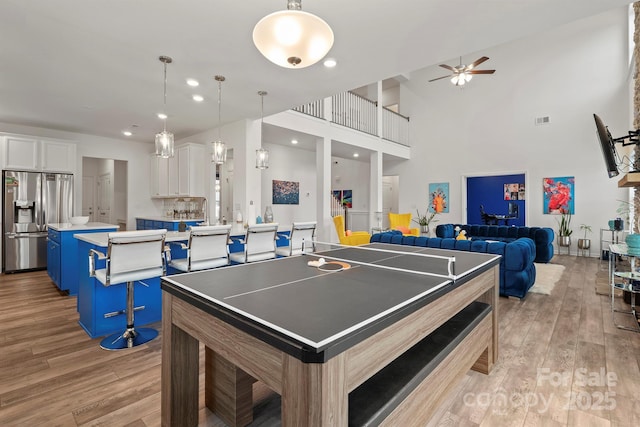 game room featuring a towering ceiling, light hardwood / wood-style floors, and ceiling fan