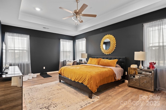 bedroom with a raised ceiling, multiple windows, and light hardwood / wood-style flooring