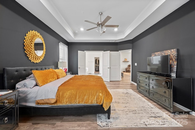 bedroom with crown molding, a tray ceiling, light hardwood / wood-style flooring, and ceiling fan