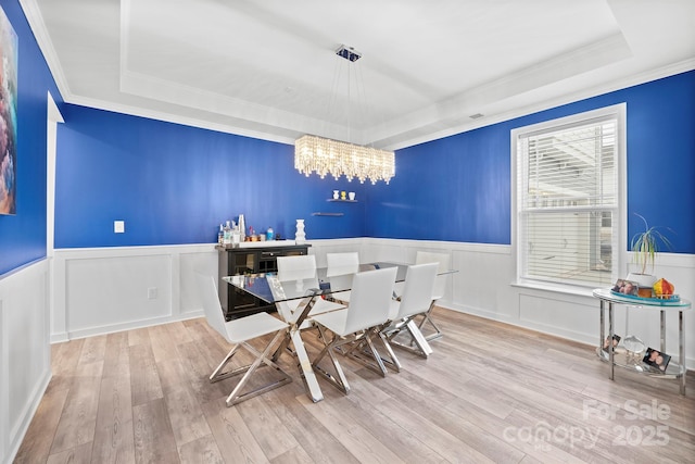 dining area featuring a raised ceiling, wood-type flooring, an inviting chandelier, and crown molding