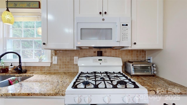 kitchen with white cabinetry, sink, hanging light fixtures, light stone countertops, and white appliances