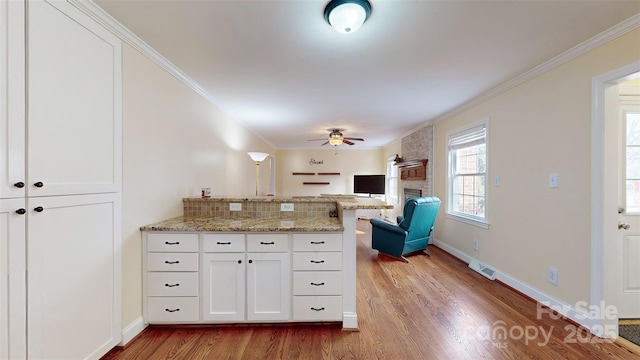 kitchen featuring crown molding, light stone countertops, white cabinets, kitchen peninsula, and light wood-type flooring