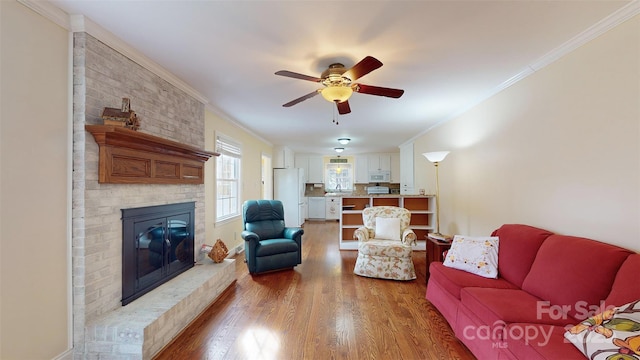 living room featuring hardwood / wood-style floors, a fireplace, sink, ornamental molding, and ceiling fan