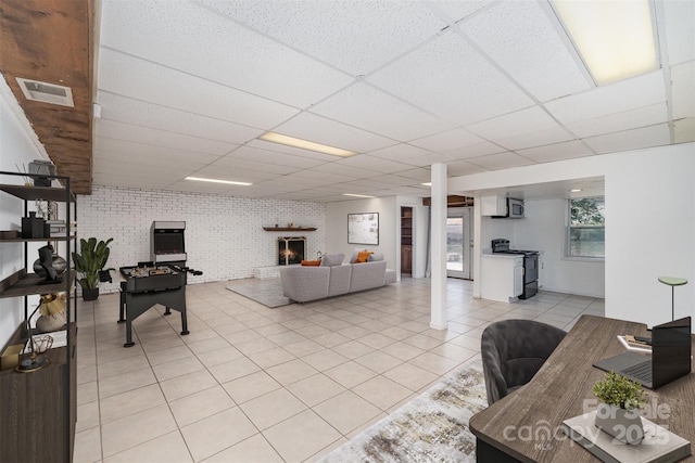 tiled living room with a paneled ceiling, a large fireplace, and brick wall