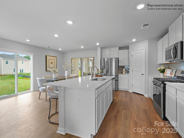 kitchen with sink, appliances with stainless steel finishes, light hardwood / wood-style floors, white cabinets, and a center island with sink