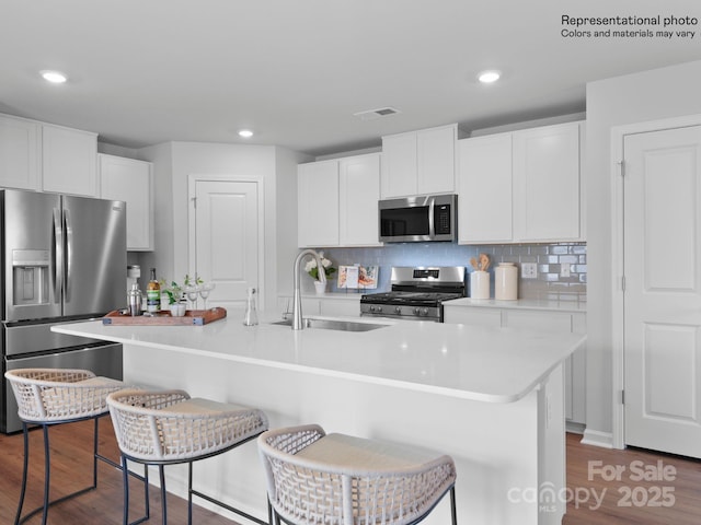 kitchen with appliances with stainless steel finishes, a breakfast bar, a center island with sink, and white cabinets