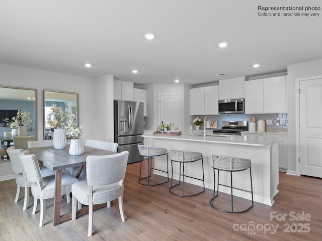 kitchen featuring appliances with stainless steel finishes, an island with sink, white cabinets, backsplash, and light hardwood / wood-style floors