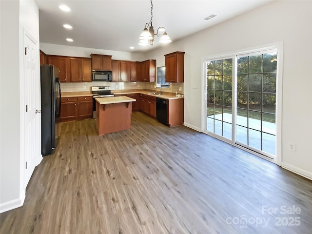 kitchen featuring hanging light fixtures, a kitchen island, a notable chandelier, hardwood / wood-style floors, and black appliances