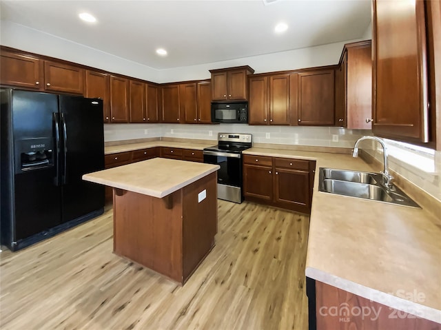 kitchen with sink, a breakfast bar area, black appliances, a kitchen island, and light wood-type flooring