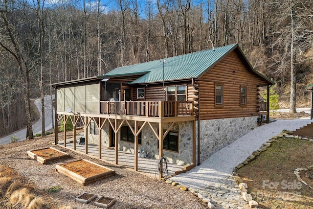 log-style house with a view of trees, stone siding, log siding, metal roof, and a wooden deck