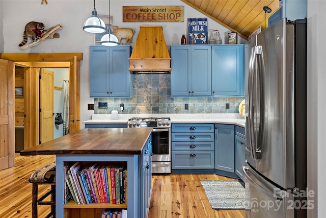 kitchen with butcher block countertops, blue cabinetry, premium range hood, appliances with stainless steel finishes, and decorative light fixtures