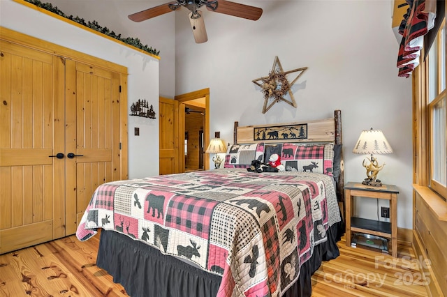 bedroom with ceiling fan, a towering ceiling, light hardwood / wood-style floors, and a closet