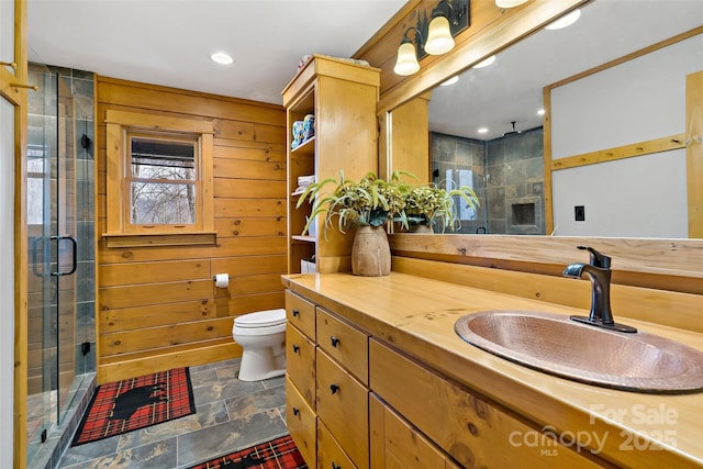 bathroom featuring toilet, stone finish flooring, wood walls, a shower stall, and vanity