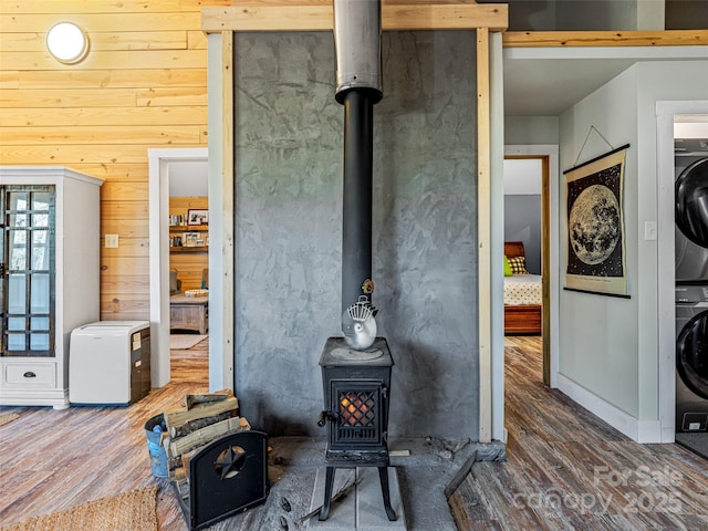 interior space featuring stacked washer and dryer, wooden walls, hardwood / wood-style floors, and a wood stove