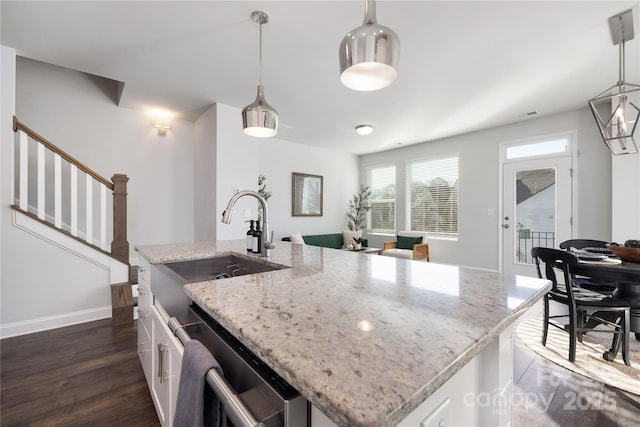 kitchen featuring a kitchen island with sink, hanging light fixtures, dishwasher, and white cabinets