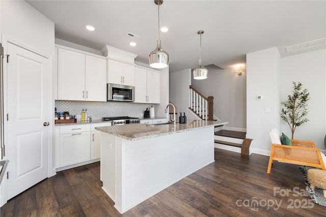 kitchen with pendant lighting, a center island with sink, white cabinets, and light stone counters