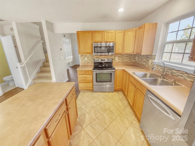 kitchen with appliances with stainless steel finishes, light brown cabinetry, sink, and backsplash