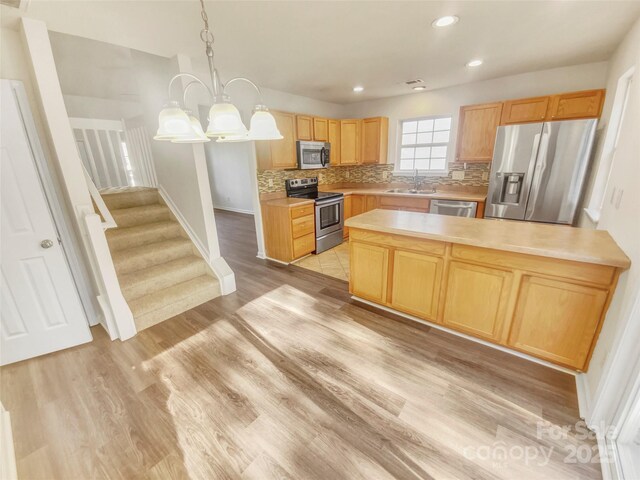 kitchen featuring sink, a center island, pendant lighting, stainless steel appliances, and light hardwood / wood-style floors