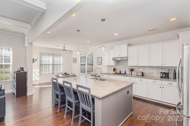 kitchen featuring pendant lighting, an island with sink, sink, stainless steel fridge, and white cabinets