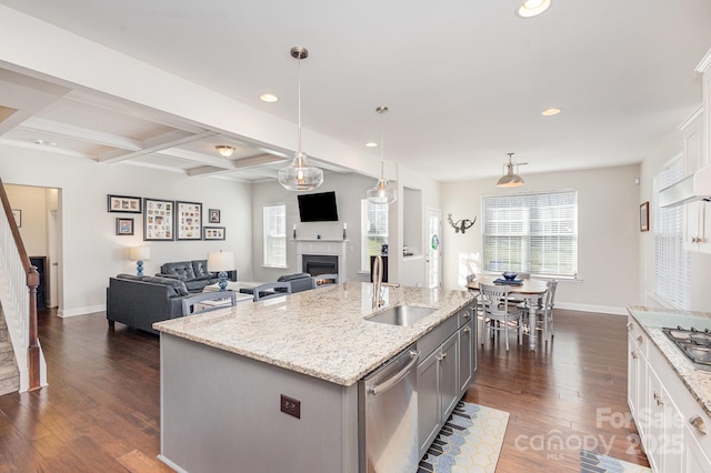 kitchen featuring pendant lighting, sink, appliances with stainless steel finishes, beam ceiling, and an island with sink