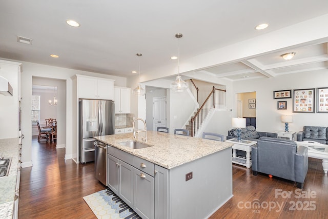 kitchen featuring sink, appliances with stainless steel finishes, beam ceiling, coffered ceiling, and an island with sink