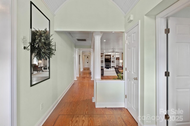 corridor with decorative columns, crown molding, lofted ceiling, and hardwood / wood-style floors