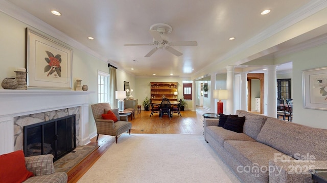 living room with crown molding, ceiling fan, a fireplace, light wood-type flooring, and ornate columns