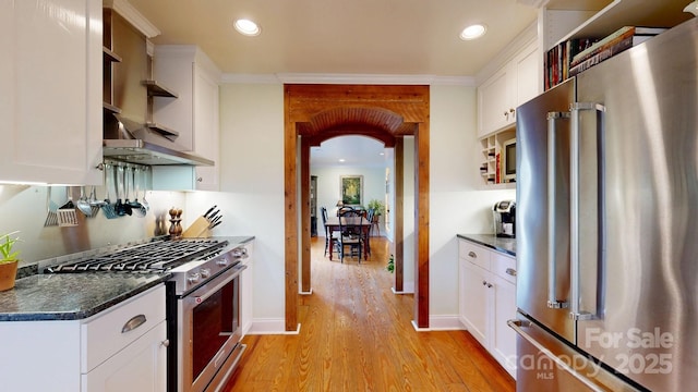 kitchen with stainless steel appliances, dark stone countertops, white cabinets, and light wood-type flooring