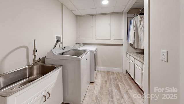 laundry room with light hardwood / wood-style floors, sink, washing machine and dryer, and cabinets