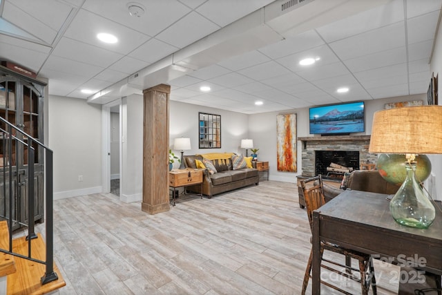 living room with a stone fireplace, a paneled ceiling, and light wood-type flooring