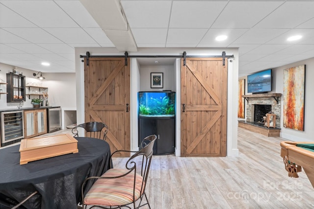 dining room featuring a barn door, a paneled ceiling, wine cooler, and light hardwood / wood-style floors