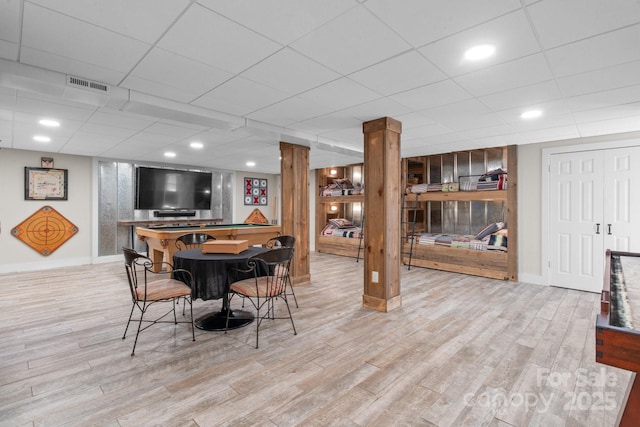 dining area with a paneled ceiling, bar area, and light hardwood / wood-style floors