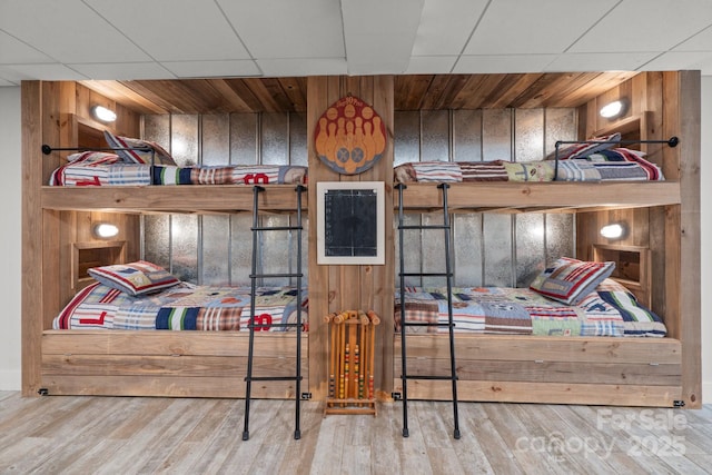 bedroom with hardwood / wood-style flooring, a paneled ceiling, and wood walls