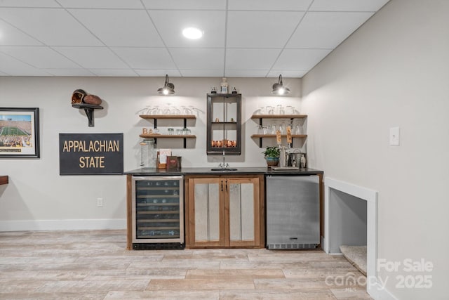 bar with stainless steel fridge, beverage cooler, light hardwood / wood-style floors, and a drop ceiling