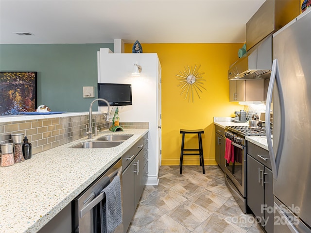 kitchen featuring stainless steel appliances, light stone countertops, sink, and decorative backsplash