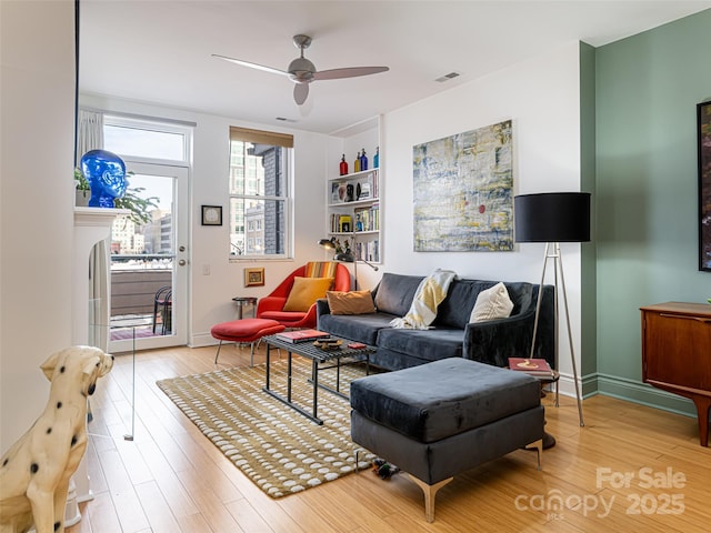 living room featuring built in shelves, a fireplace, light hardwood / wood-style floors, and ceiling fan