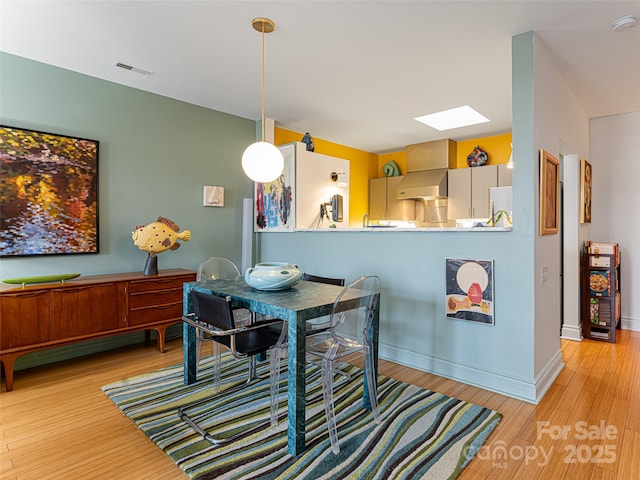 dining space featuring light wood-type flooring and a skylight