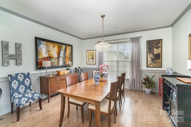 dining space with ornamental molding, a notable chandelier, and light wood-type flooring