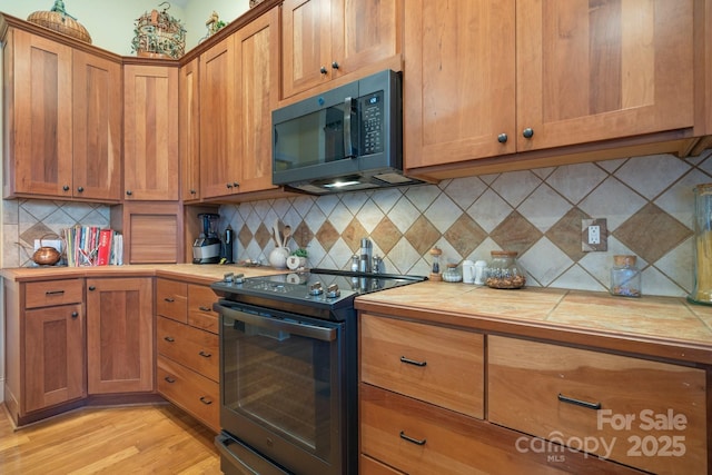 kitchen with tile countertops, black electric range oven, decorative backsplash, and light wood-type flooring