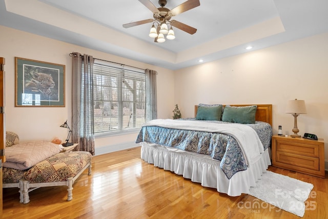 bedroom with a raised ceiling, ceiling fan, and light wood-type flooring