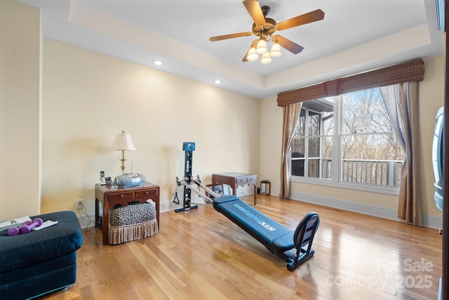 exercise room with hardwood / wood-style floors, a tray ceiling, and ceiling fan