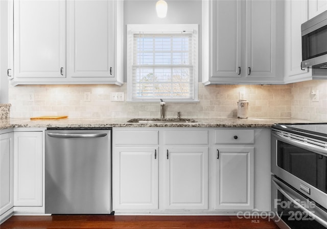 kitchen with light stone counters, stainless steel appliances, backsplash, white cabinets, and a sink